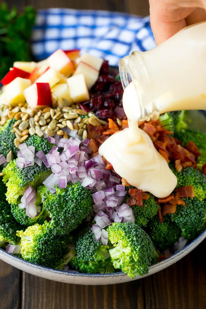 Creamy dressing being poured over a bowl of broccoli salad ingredients.