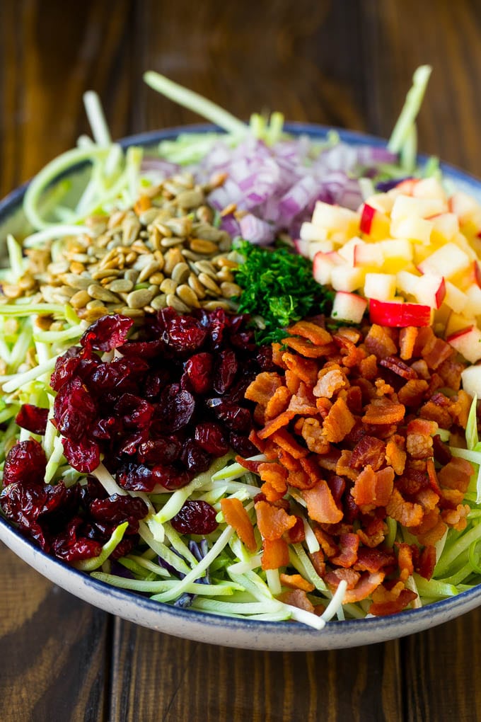 Broccoli slaw, bacon, apples, onion, sunflower seeds and parsley in a bowl.