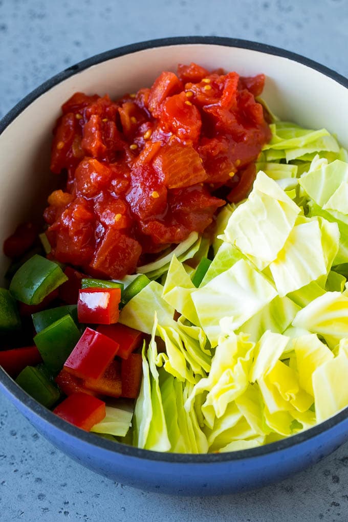 Red and green peppers, diced tomatoes and raw veggies in a large pot.