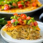 A slice of cheeseburger pie garnished with shredded lettuce, diced tomatoes and pickles.