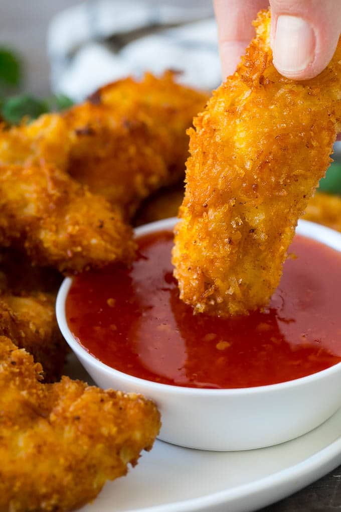 A hand dipping coconut chicken into sweet chili sauce.