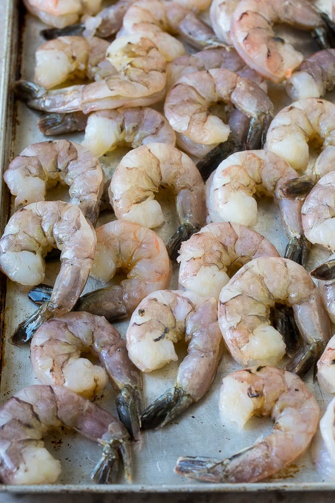 Large raw tail-on shrimp arranged on a sheet pan.