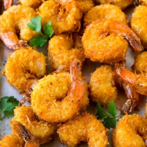 A pile of crispy coconut shrimp on a sheet pan with cilantro leaves for garnish.