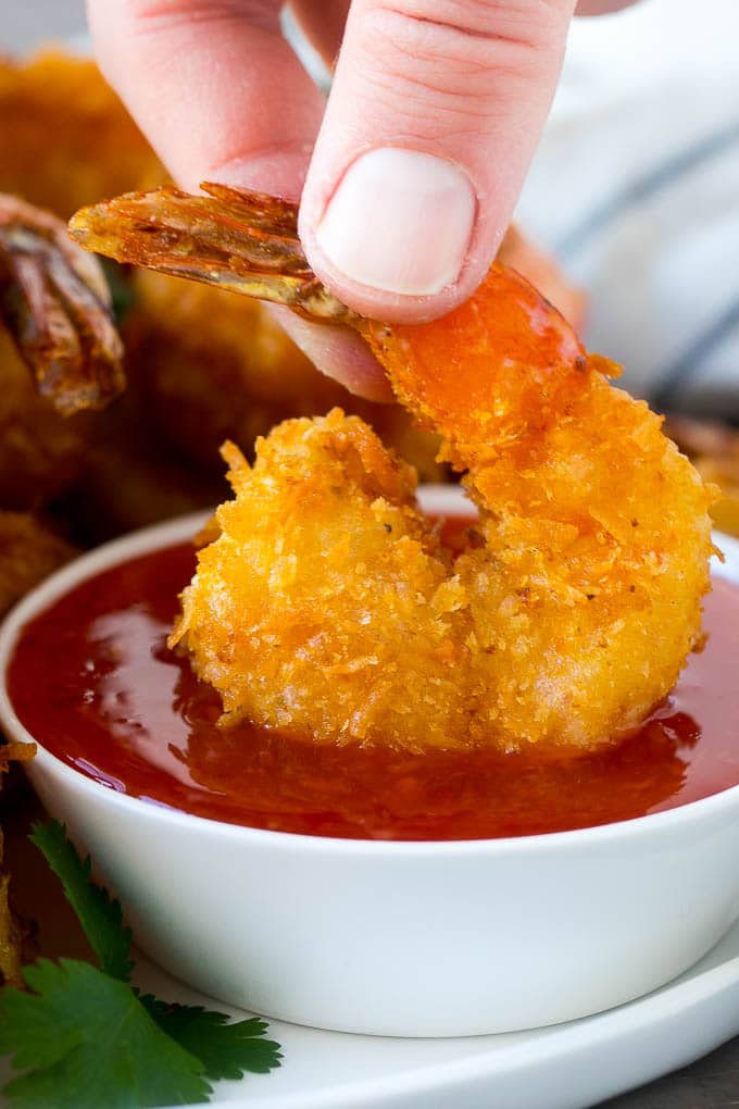 A hand dipping a crispy prawn into a bowl of sweet chili sauce.