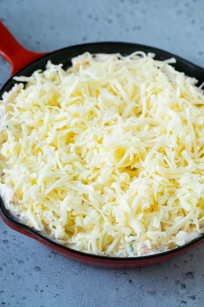 A skillet of corn dip covered with shredded cheese.