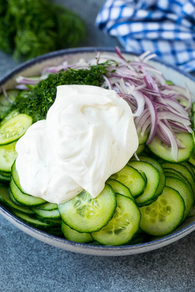 Cucumbers, red onion and dill in a bowl topped with creamy dressing.