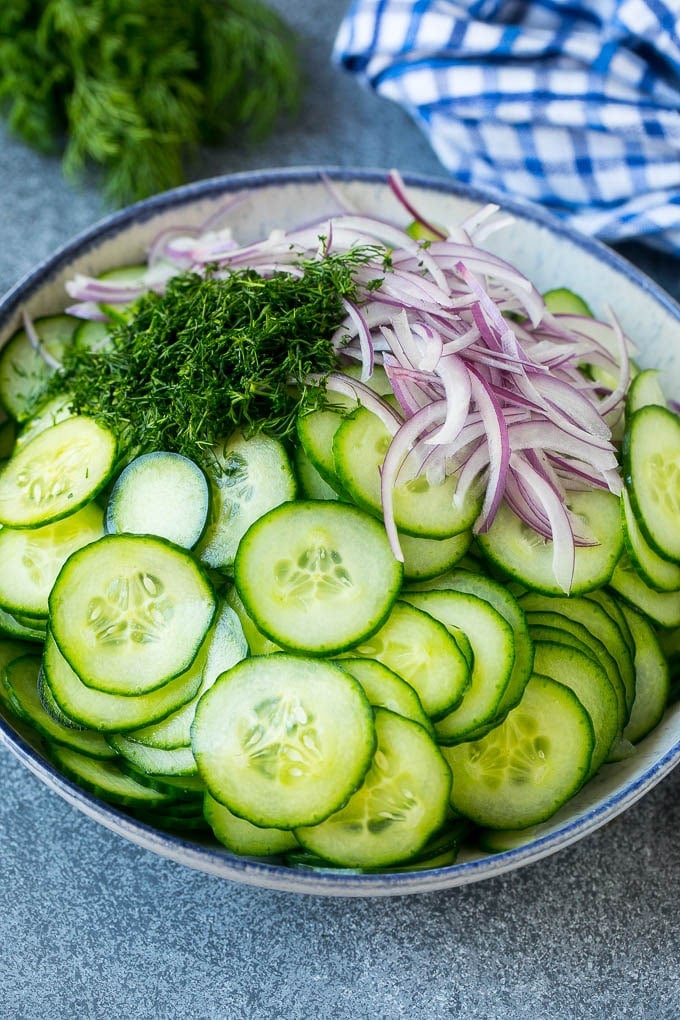 Thinly sliced cucumbers, red onion and fresh dill in a mixing bowl.