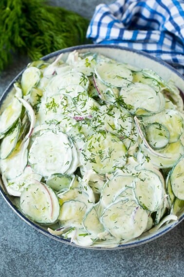 Creamy cucumber salad with red onion and dill, topped with fresh herbs for garnish.