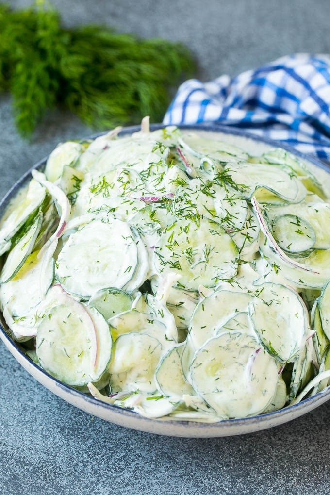 A serving bowl of creamy cucumber salad topped with fresh dill.