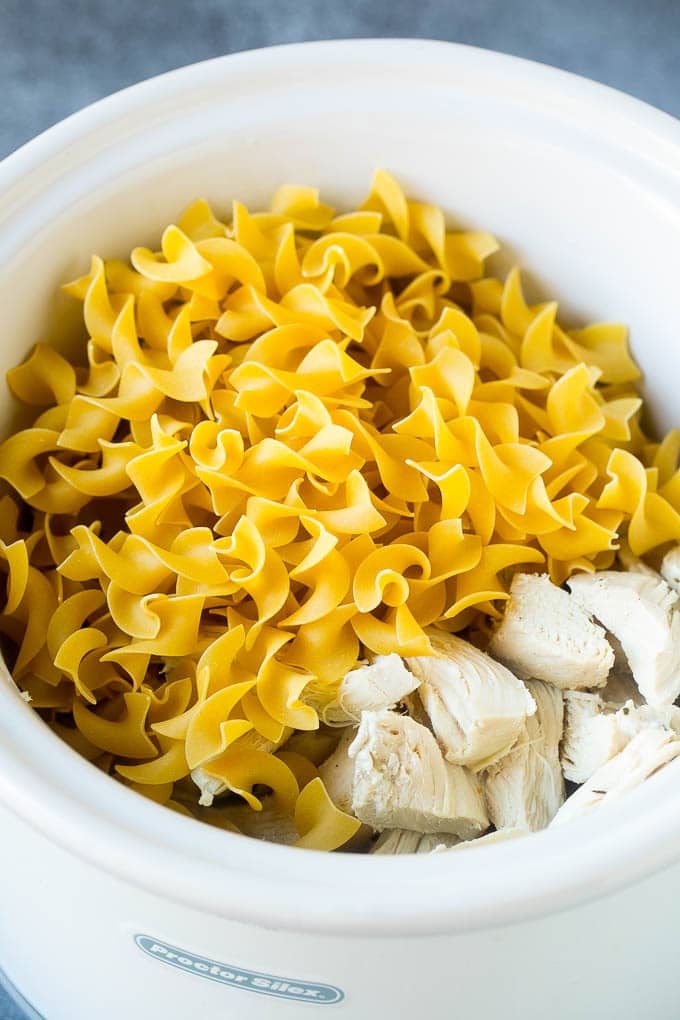 Egg noodles and shredded chicken in a crock pot full of soup.