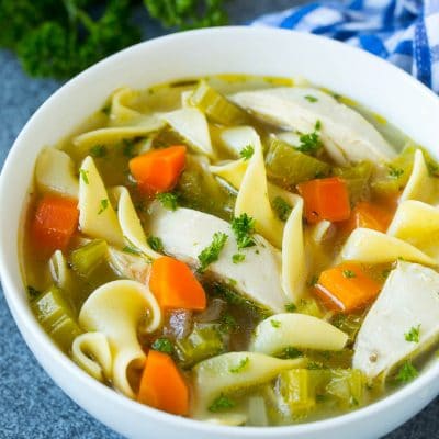 A bowl of crock pot chicken noodle soup with carrots, garnished with parsley.