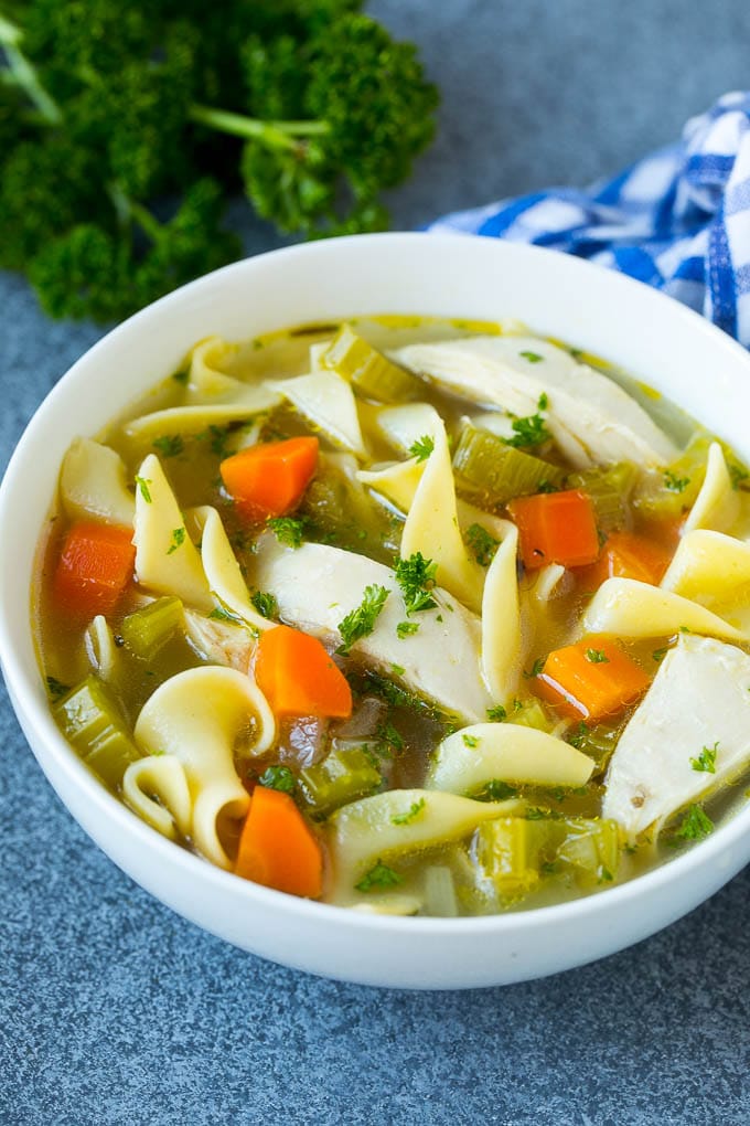 A bowl of crock pot chicken noodle soup with carrots, garnished with parsley.