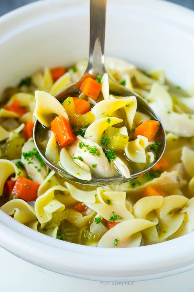 A ladle full of crock pot chicken noodle soup inside a slow cooker.