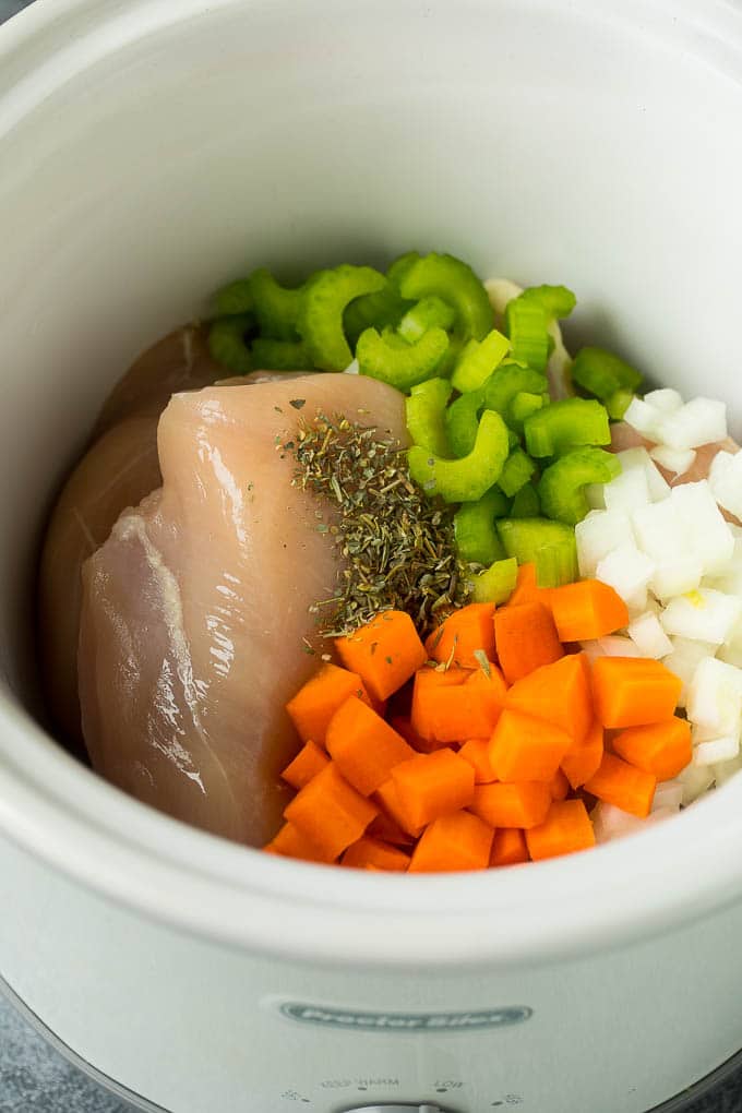 Chicken breasts, seasonings, carrots, onion and celery in a slow cooker.