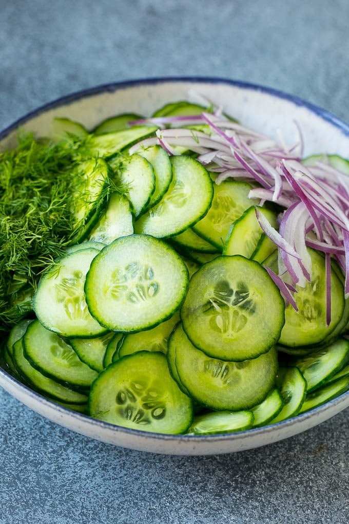 Thinly sliced cucumbers, red onion and dill in a bowl.
