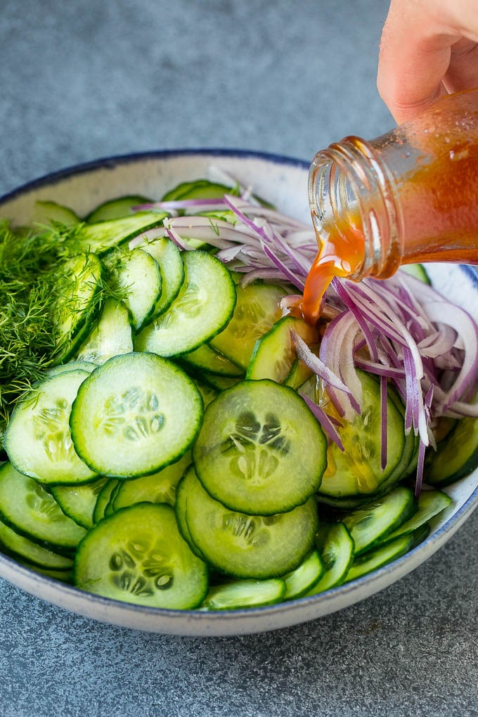 Dressing being poured over sliced cucumbers, red onion and fresh dill.