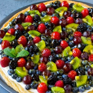 Fruit pizza with a sugar cookie crust and cream cheese frosting, topped with berries, kiwi and grapes.