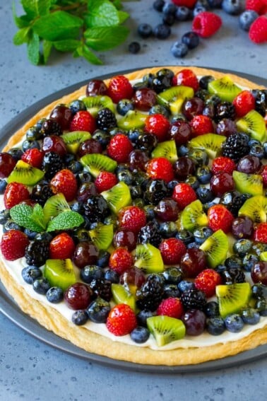 Fruit pizza with a sugar cookie crust and cream cheese frosting, topped with berries, kiwi and grapes.