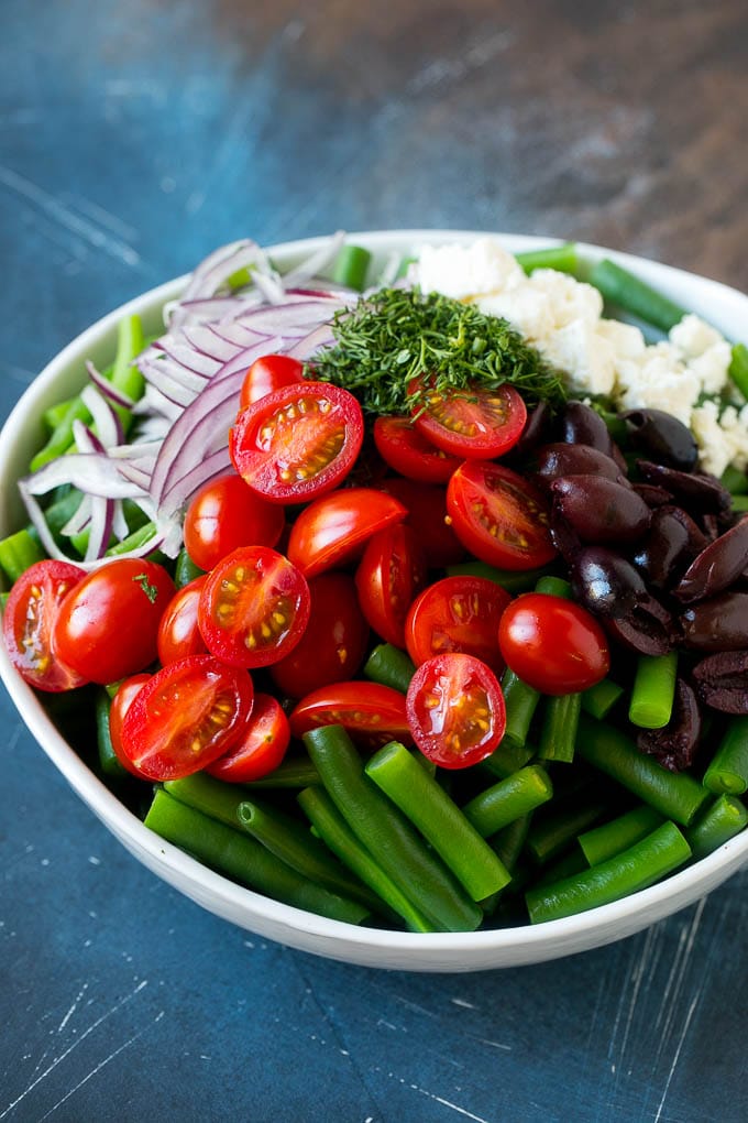 Green beans, cherry tomatoes, red onion, olives and feta cheese in a bowl.