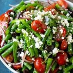 A bowl of green bean salad made with feta cheese, tomatoes, red onion and kalamata olives.