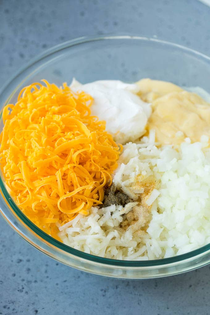 A bowl of potato shreds, cheese, cream of chicken soup, sour cream and seasonings.