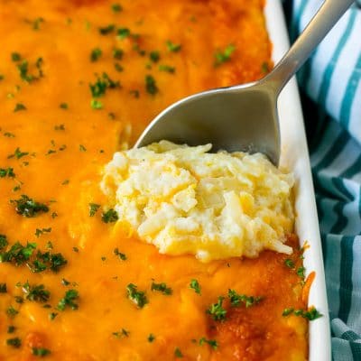 Hash brown casserole with potatoes, cheddar cheese, onions and sour cream, with a serving spoon in the dish.