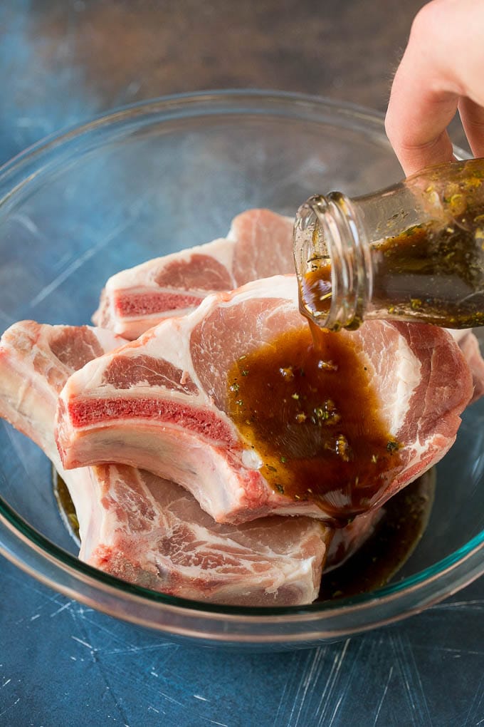 Pork chops in a bowl with marinade being poured over them.