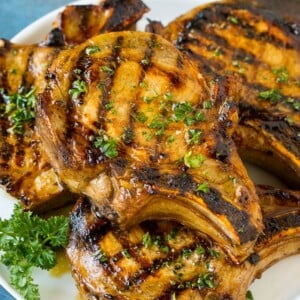 Pork chop marinade on grilled pork chops. The pork chops are on a serving plate garnished with parsley.