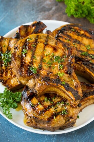 Pork chop marinade on grilled pork chops. The pork chops are on a serving plate garnished with parsley.
