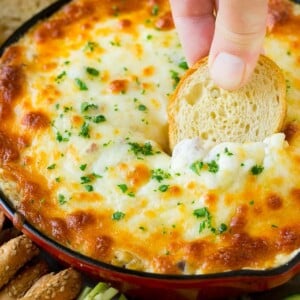 A hand scooping out a serving of Reuben dip with baguette.