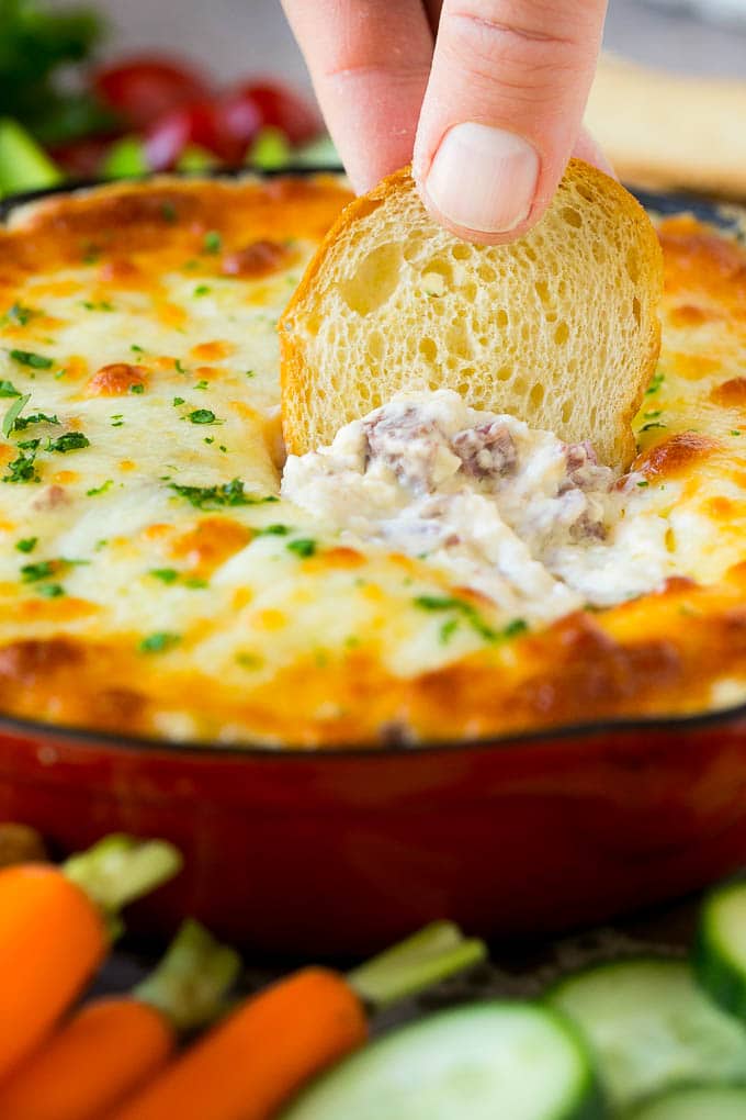 A baguette chip dipping into a skillet of Reuben dip.