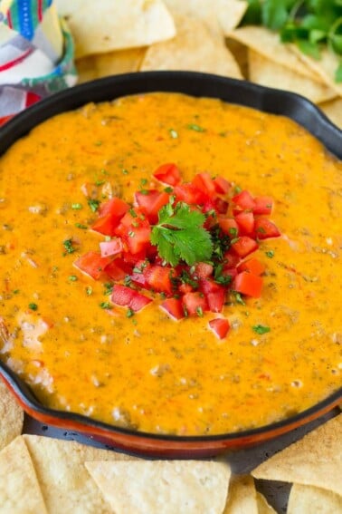 A skillet of Rotel dip topped with fresh tomatoes and cilantro, served with tortilla chips.