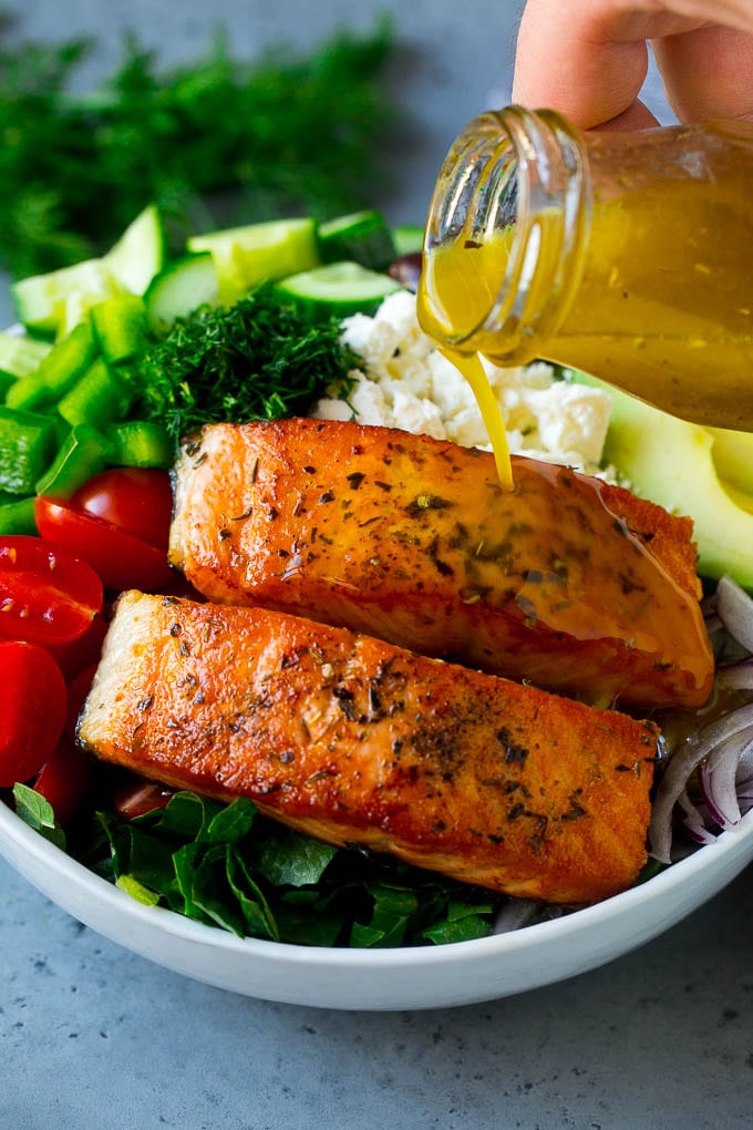 Salmon fillets on top of greens with dressing being poured over the top.