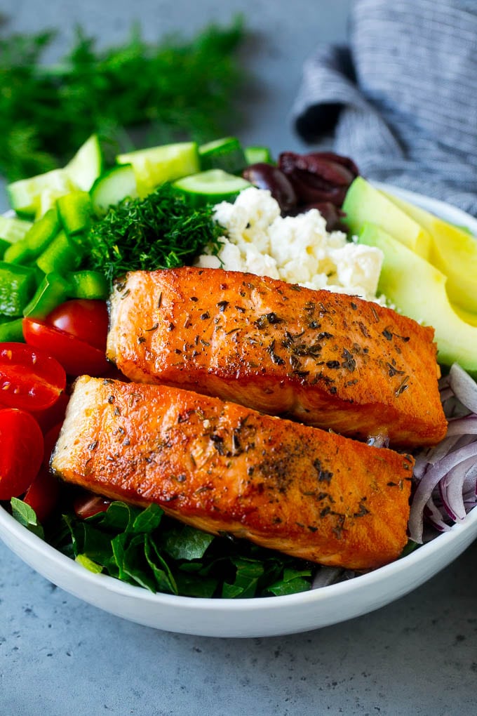 Salmon fillets on lettuce with tomatoes, feta cheese, avocado, olives, cucumbers and herbs.