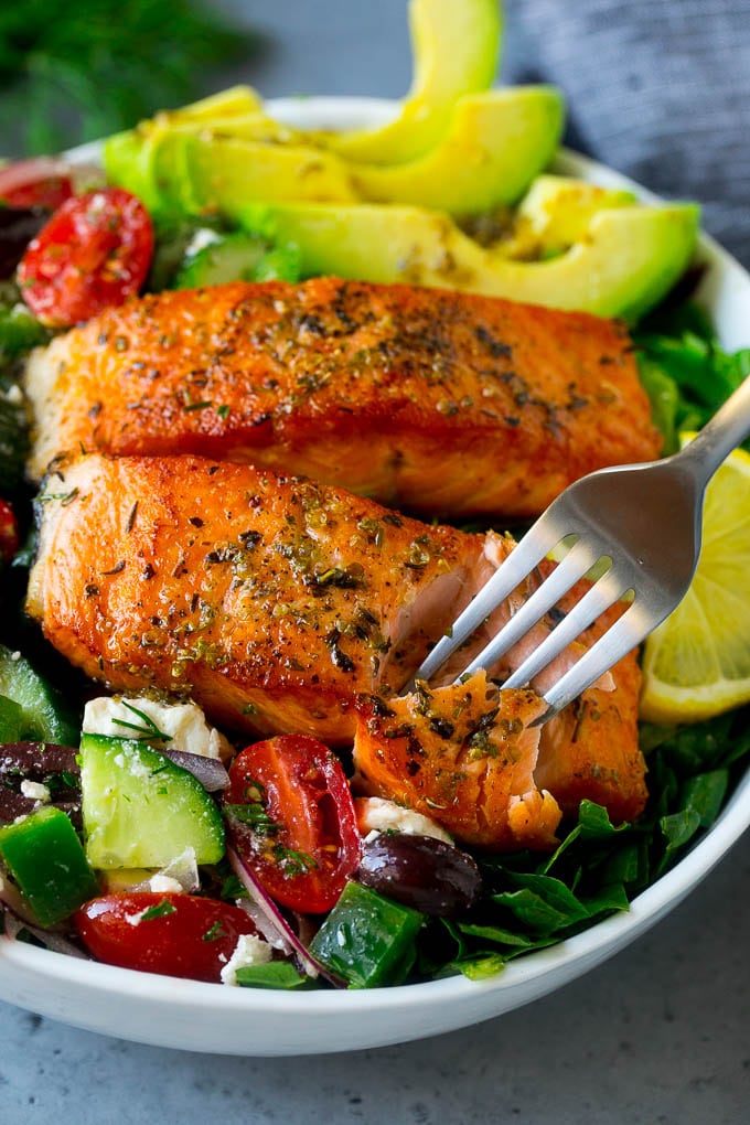 A fork cutting into a salmon fillet in Greek salmon salad.