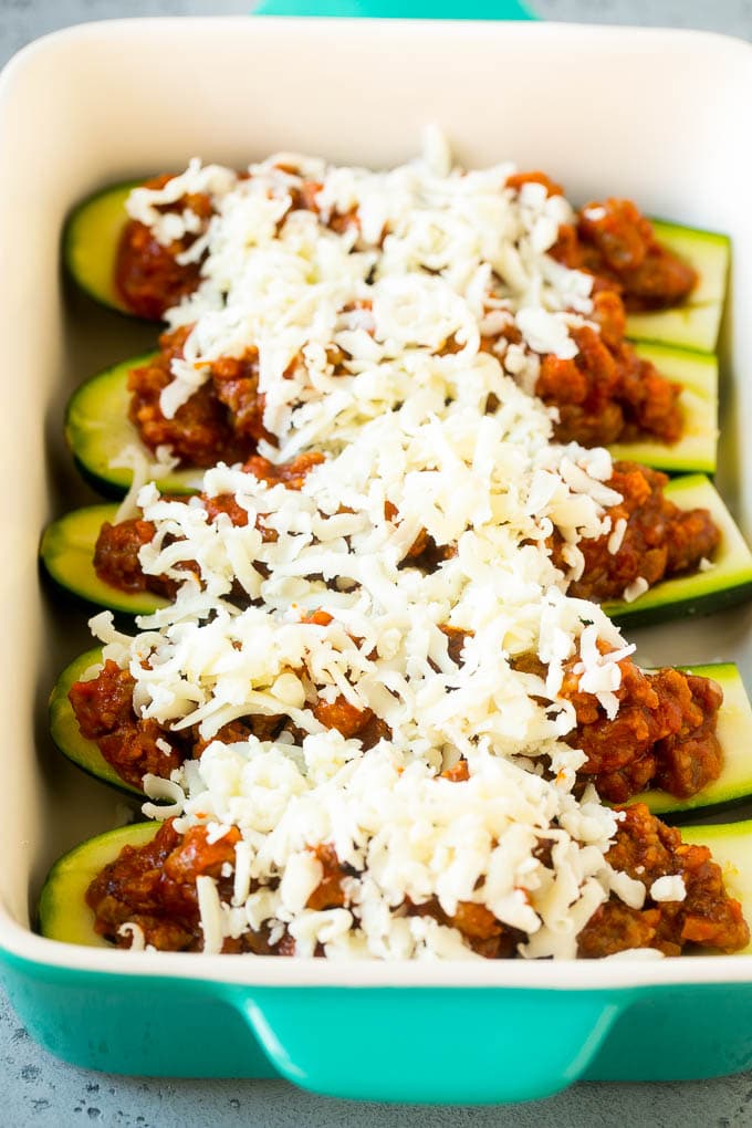 Zucchini boats in a baking dish with meat sauce and shredded cheese.