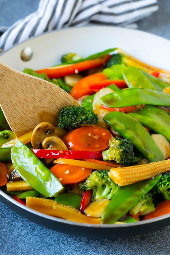 A spatula in a pan of veggie stir fry with carrots, snow peas and broccoli.