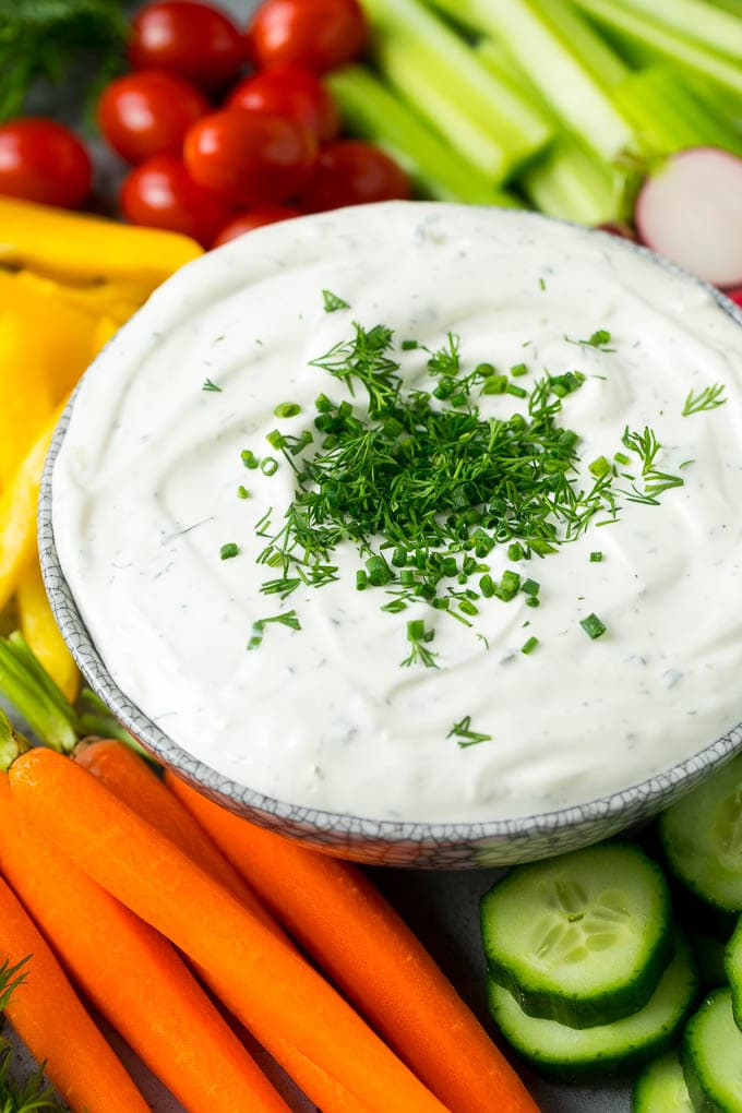 A bowl of veggie dip surrounded by an assortment of fresh vegetables.