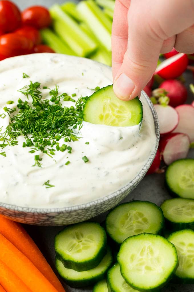 A hand scooping up veggie dip with a cucumber slice.