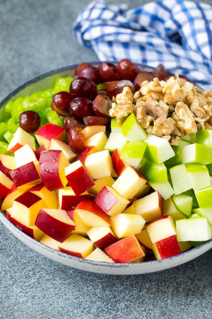 Red and green apples, grapes, walnuts and celery in a serving bowl.