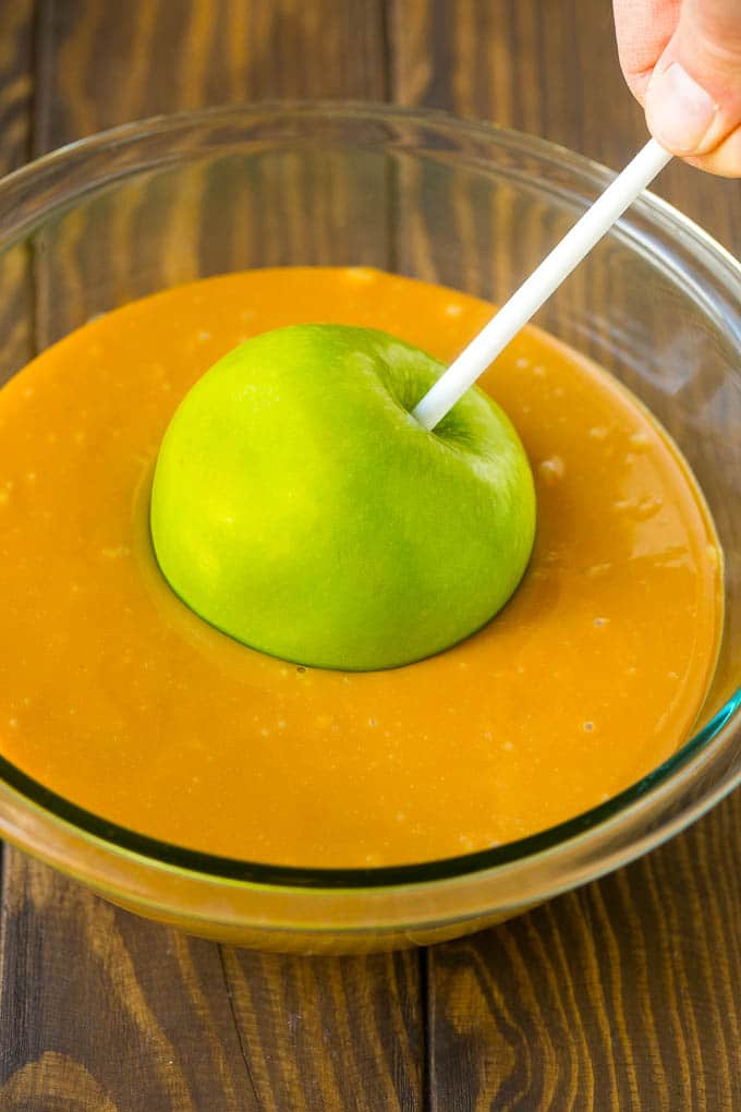 A green apple being dipped into a bowl of melted caramel.