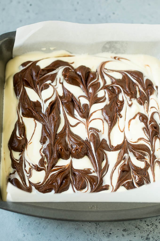 Swirled chocolate and cream cheese brownie batters in a baking pan.
