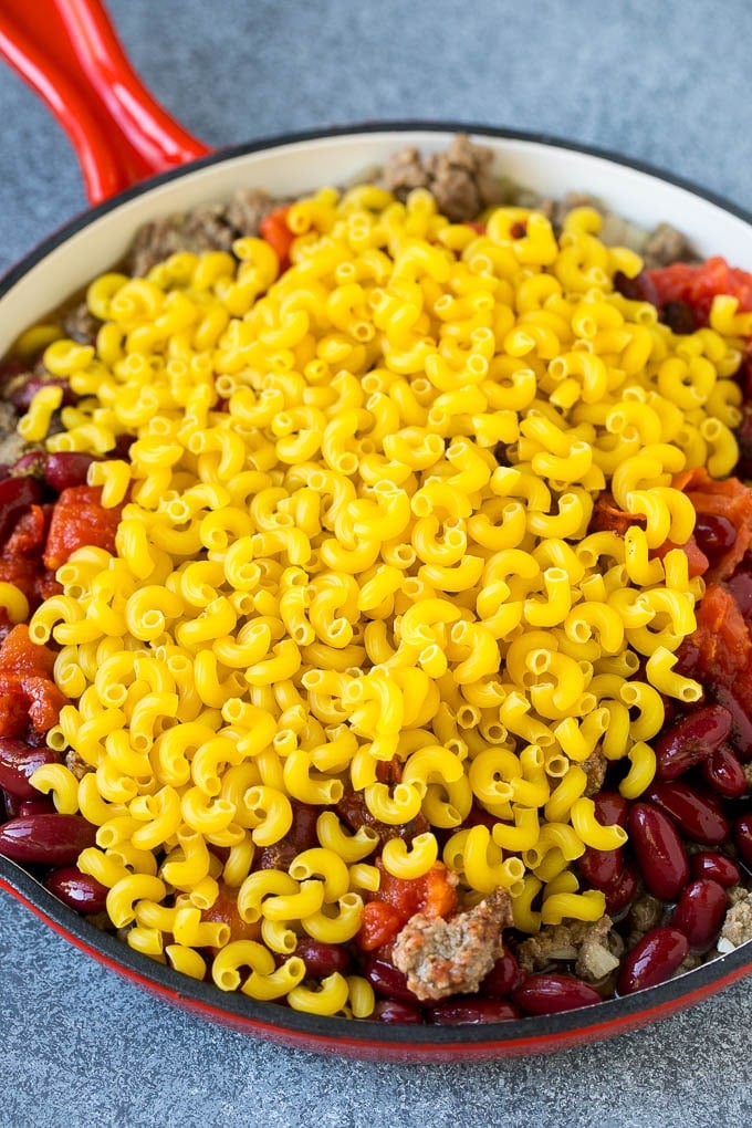 Uncooked macaroni in a skillet with ground beef and tomatoes.