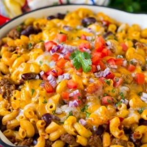 A skillet of chili mac topped with melted cheese, diced tomatoes and minced onion.