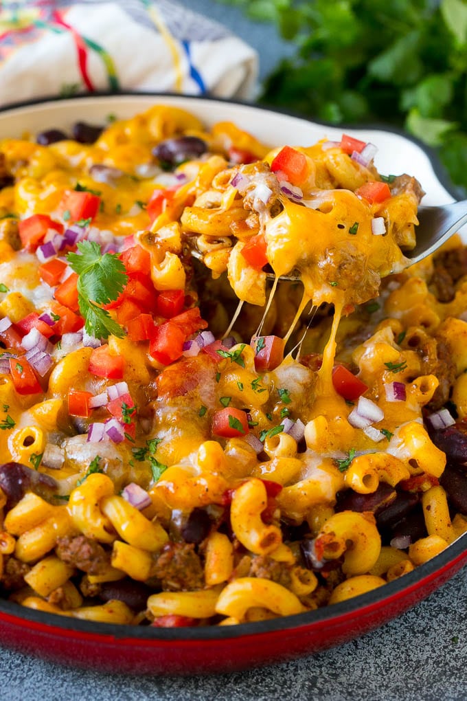 A serving spoon in a pan of chili mac scooping up a portion.