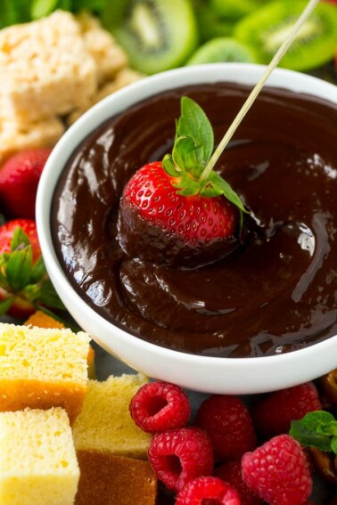 A strawberry on a skewer dipped into a bowl of chocolate fondue.