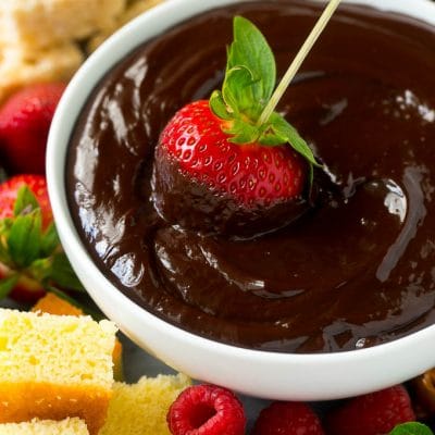 A strawberry on a skewer dipped into a bowl of chocolate fondue.