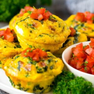 Breakfast egg muffins on a serving plate garnished with tomato and herbs.