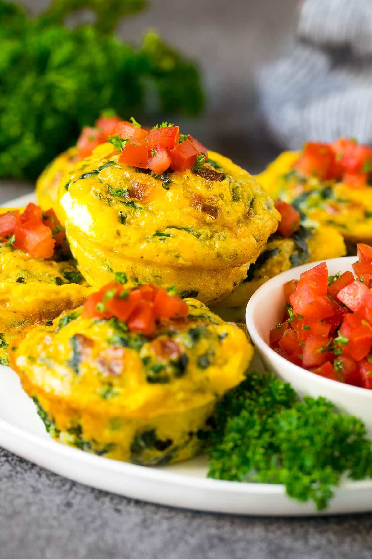 Breakfast egg muffins on a serving plate garnished with tomato and herbs.