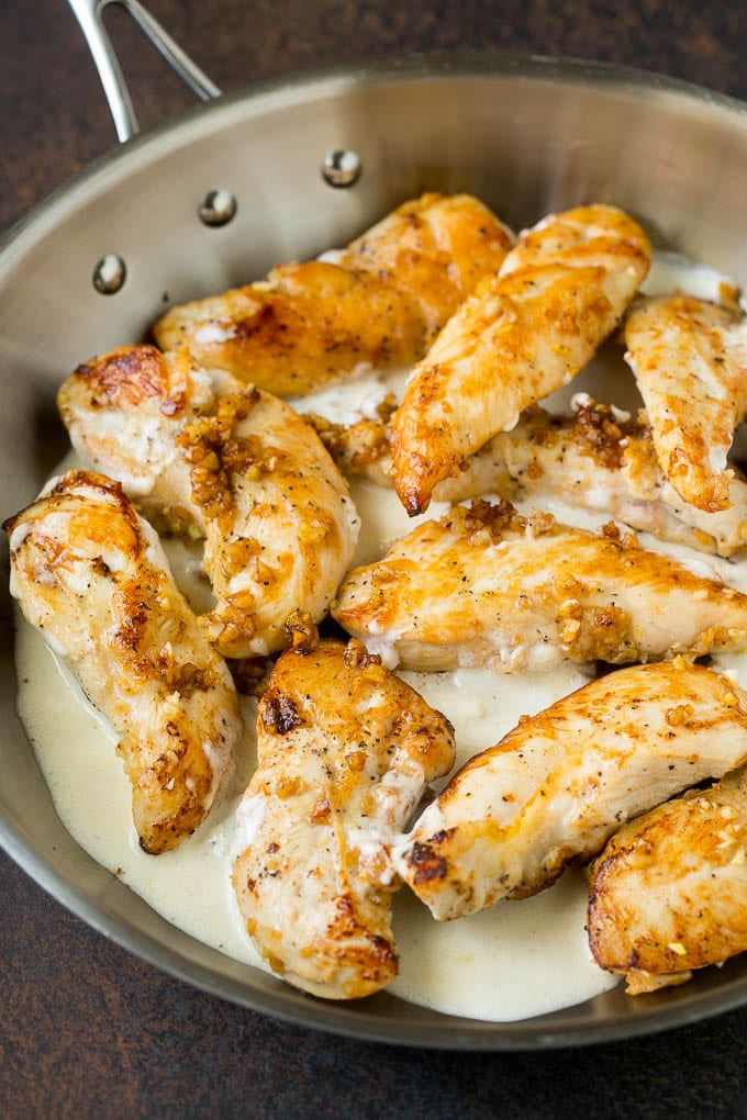 Sauteed chicken breast tenders in a pan of cream sauce.